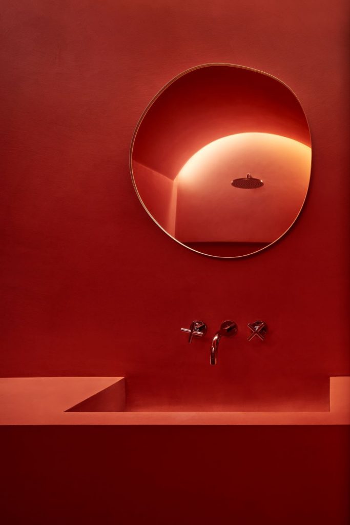 Dočervena sfarbená kúpeľňa s umývadlom a zrkadlom v nepravidelnom tvare.