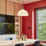 Časť kuchyne s drevenou linkou i jedálenským stolom, červenou stenou, zelenou zástenou a čiernymi stoličkami.