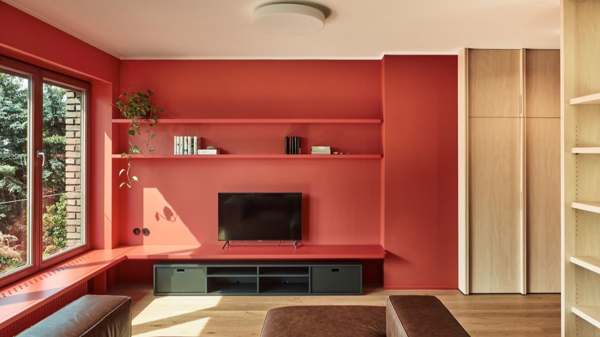 bývačka s dvoma červenými stenami s červenými policami, čiernou skrinkou pod televízorom a hnedou sedačkou.