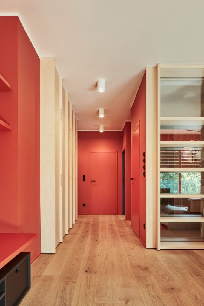 Chodba s drevenými parketami a červenými stenami s dverami v rovnakej farbe.