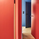 Chodba s drevenou podlahou a červenými i modrými stenami s rovnako farebne zladenými dverami.