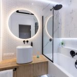 Kúpeľňa s okrúhlym podsvieteným zrkadlom nad umývadlom na doske.