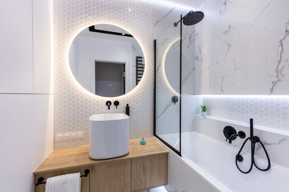 Kúpeľňa s okrúhlym podsvieteným zrkadlom nad umývadlom na doske.