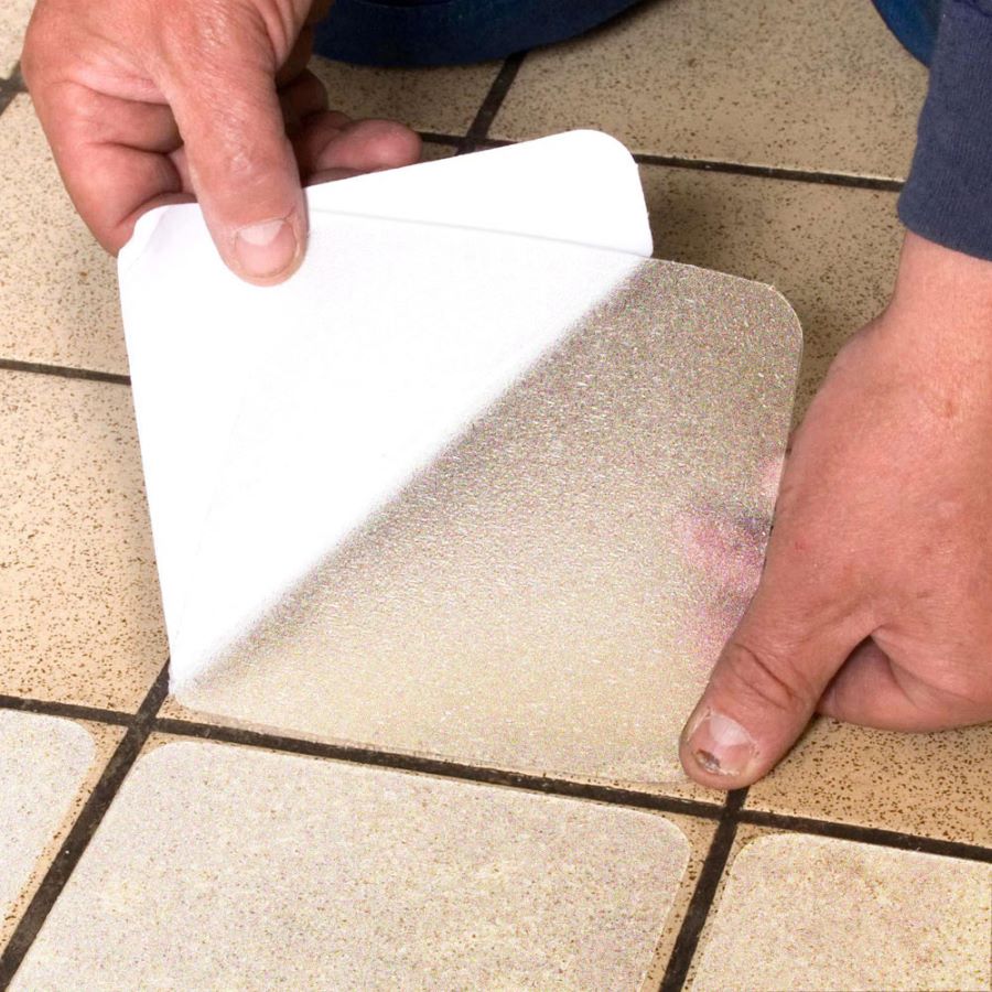 Človek lepí protišmykovú samolepiacu dlaždicu na podlahu.