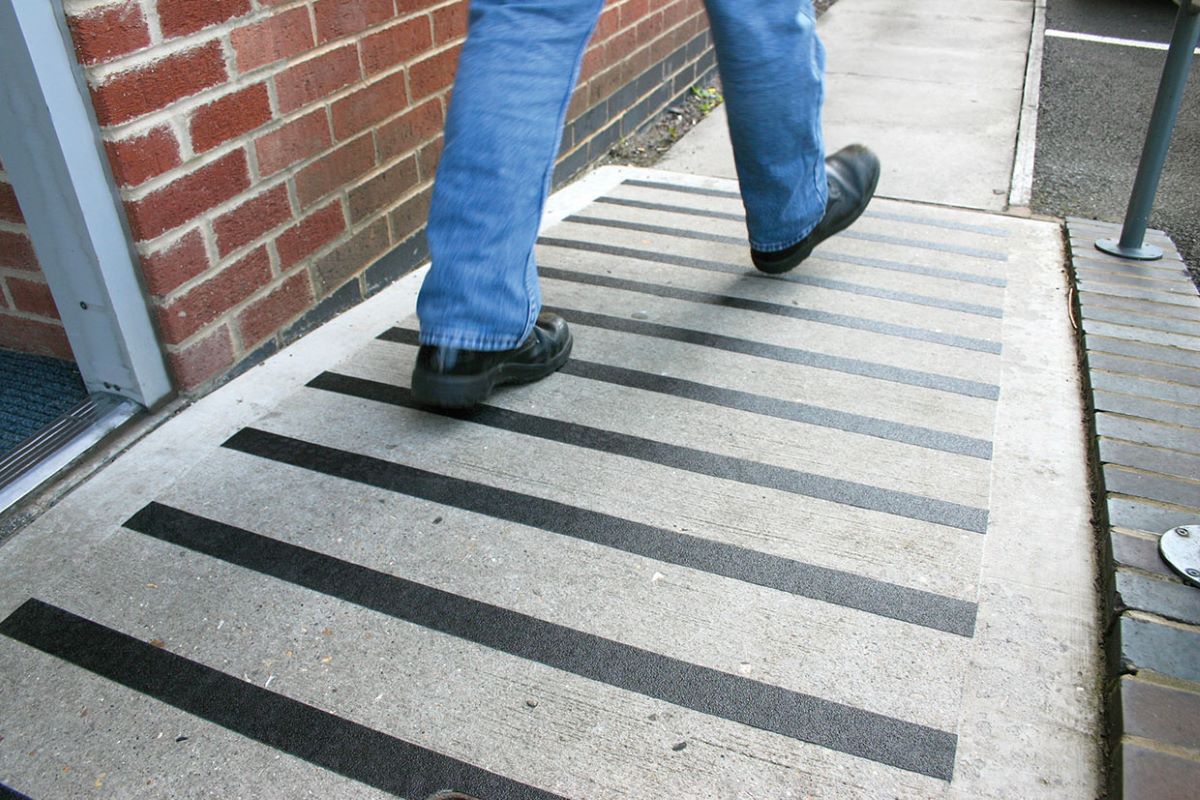 Muž kráča po naklonenom betónovom chodníku s protišmykovými páskami.