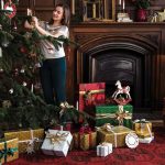 Žena vešia ozdoby na vianočný stromček, pod ktorým sú darčeky.