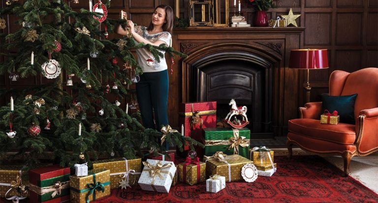 Žena vešia ozdoby na vianočný stromček, pod ktorým sú darčeky.