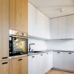 Časť kuchyne s bielou kuchynskou linkou a dreveným úložnými priestorom.