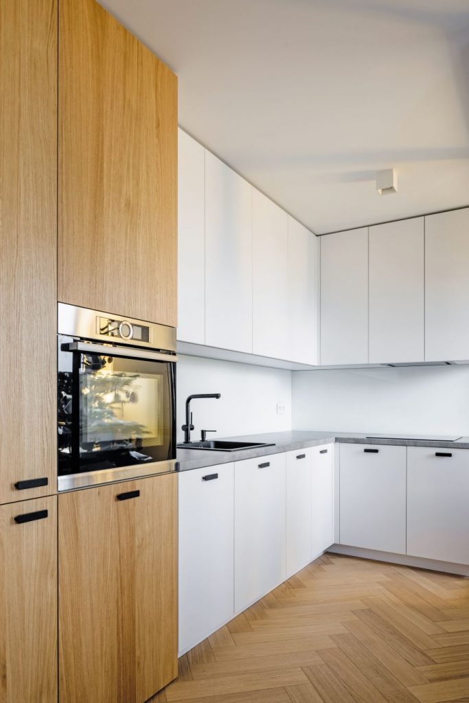 Časť kuchyne s bielou kuchynskou linkou a dreveným úložnými priestorom.
