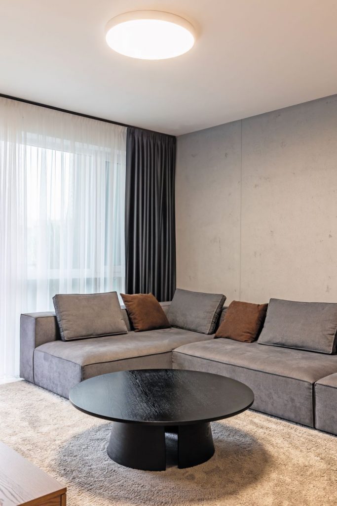 Časť obývačky so sivou sedačkou a okrúhlym stolíkom.