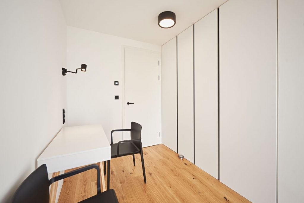 Minimaliasticky zariadená miestnosť v dome s úložným priestorom, stolom a stoličkami.