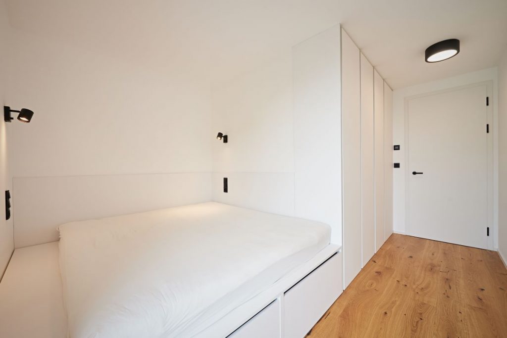 Minimalisticky zariadená miestnosť v dome s posteľou a úložným priestorom.