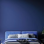 Záber na manželskú posteľ v námorníckej modrej pri tmavomodrej stene.