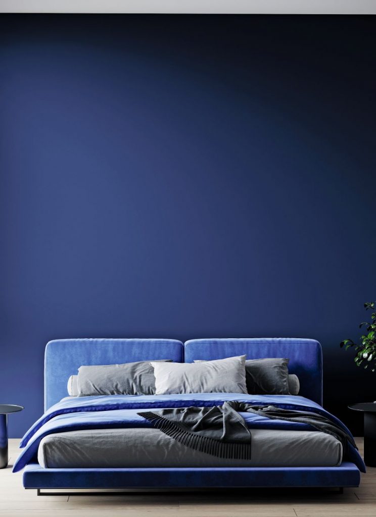 Záber na manželskú posteľ v námorníckej modrej pri tmavomodrej stene.