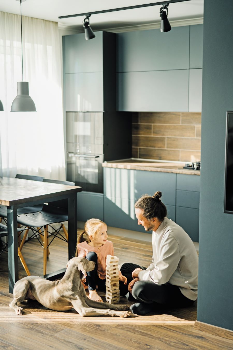 Muž s dievčaťom a psom sedia v kuchyni na podlahe.