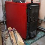 Starý boiler v červeno-čiernej farbe, na ktorom spí mačka.