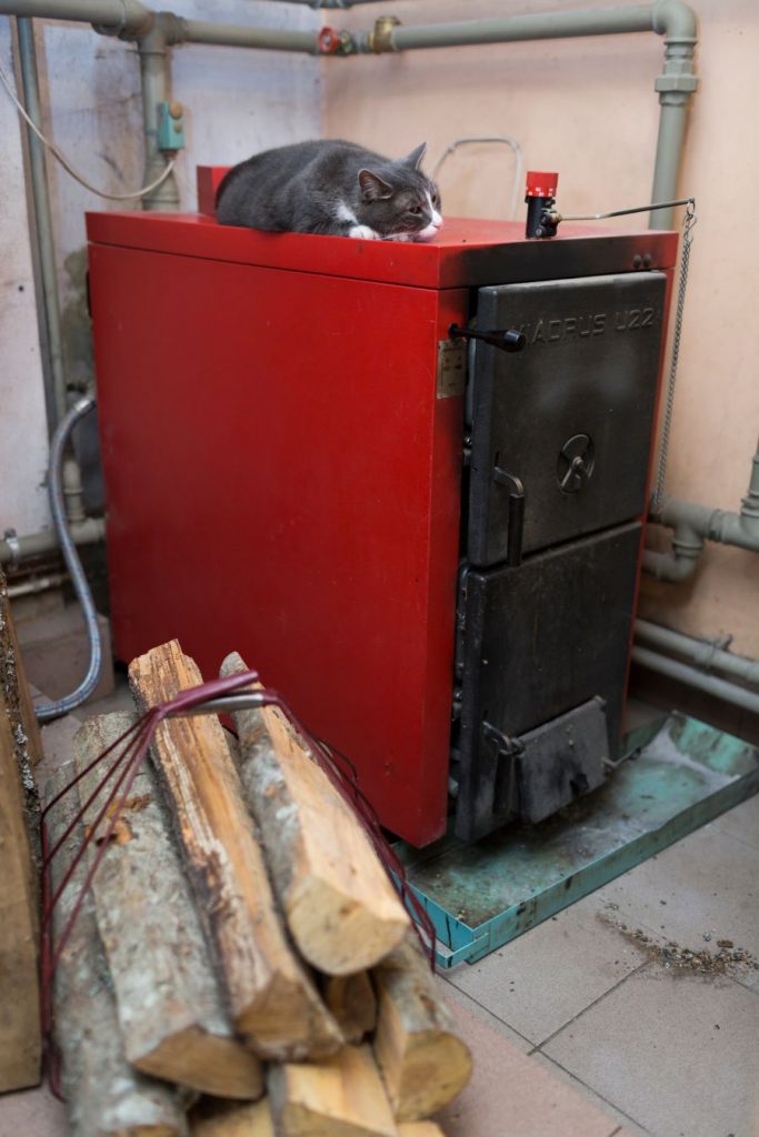 Starý boiler v červeno-čiernej farbe, na ktorom spí mačka.