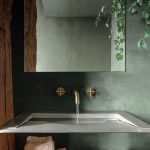 Časť kúpeľne so zelenkavými stenami a hranatým umývadlom aj zrkadlom.