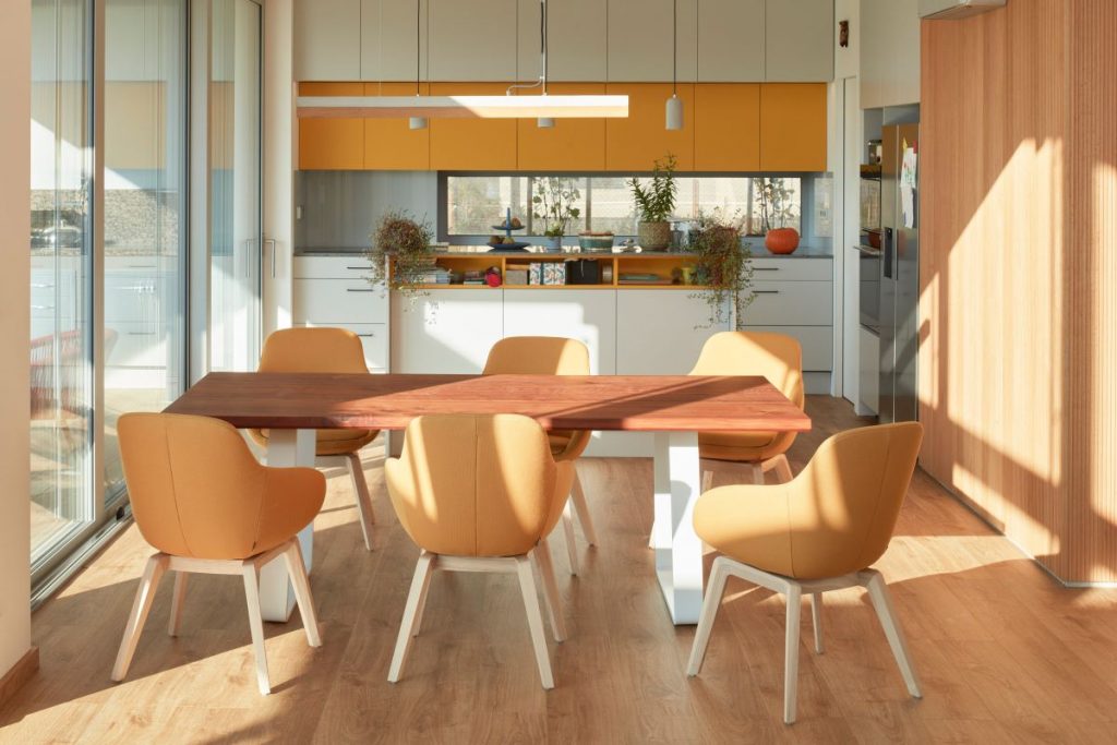 Jedálenský stôl so stoličkami pri oranžovo-bielej kuchynskej linke.