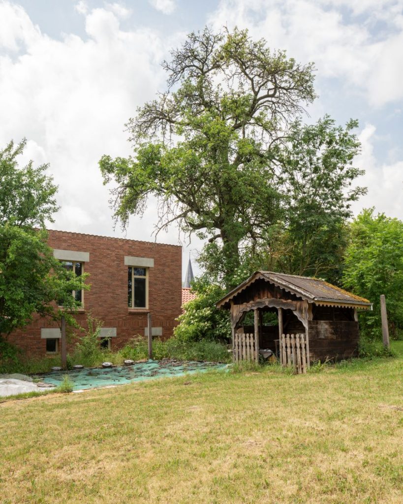 Pohľad na dvor pri tehlovom dome House W s dreveným altánkom.