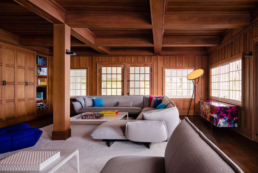 Obývačka obložená drevom so sivým kobercom aj sedačkou.