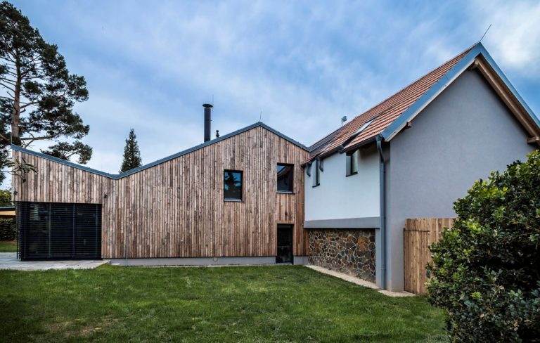 Dve rozdielne hmoty rodinného domu v Prahe s drevenou fasádou domu a omietnutou pôvodnou stodolou.
