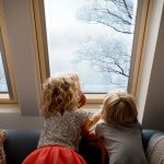 Dve deti sa dívajú von strešným oknom na zimnú krajinu.