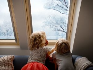 Dve deti sa dívajú von strešným oknom na zimnú krajinu.