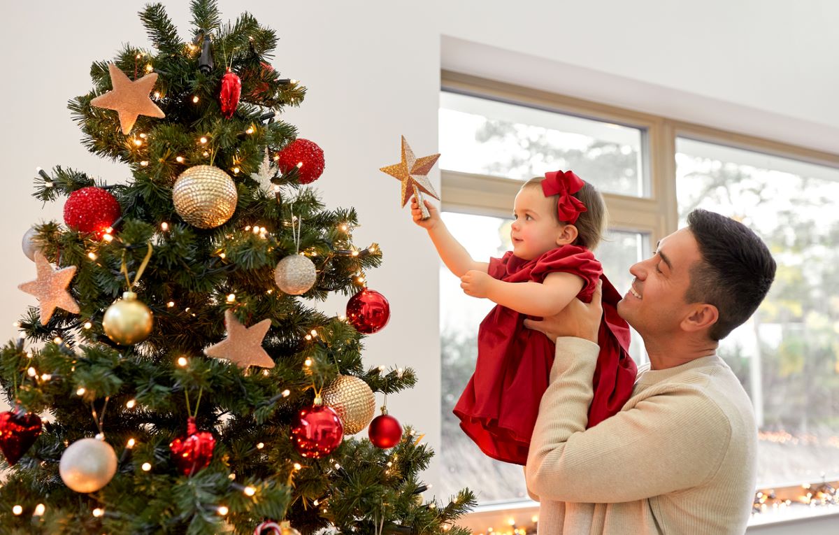 Muž dvíha malé dievčatko s vianočnou hviezdou k vianočnému stromčeku.