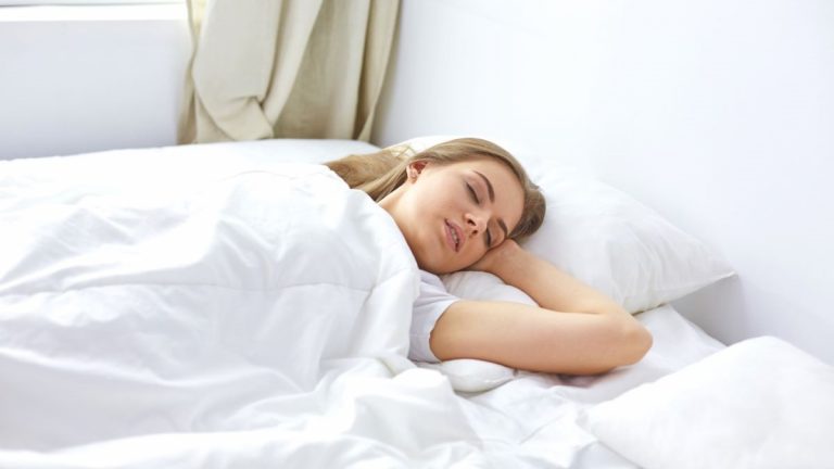 Žena spiaca na posteli s bielymi obliečkami.