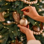 Ženské ruky vešajú vianočnú guľu na vianočný stromček.