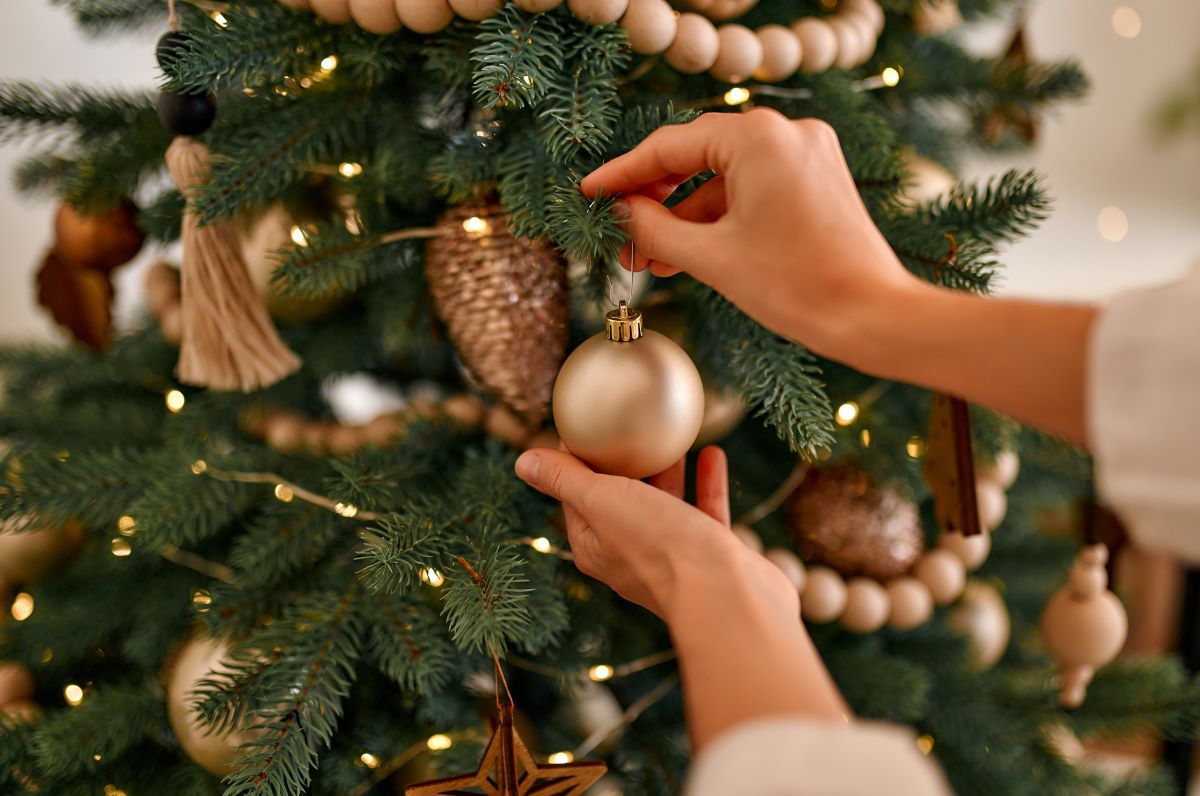 Ženské ruky vešajú vianočnú guľu na vianočný stromček.