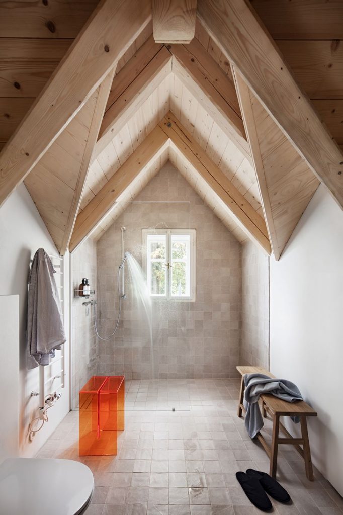 Minimalisticky zariadená kúpeľňa v chalupe so sprchovacím kútom a drevenou lavicou.