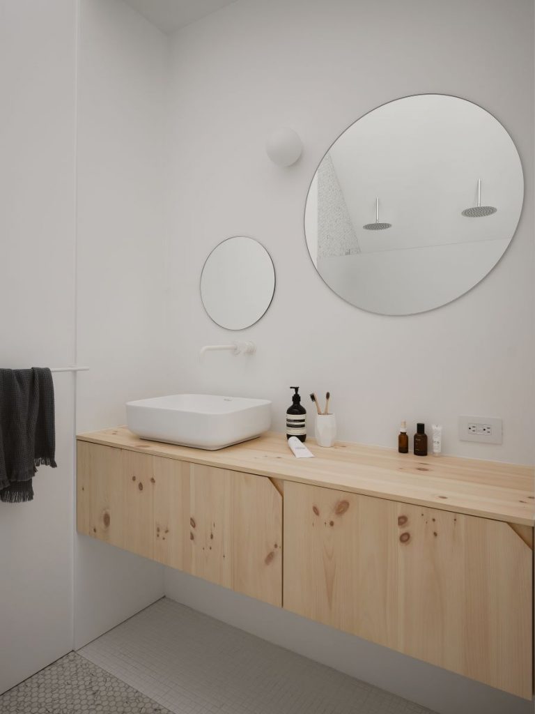 Časť kúpeľne v chate v minimalistickom prevedení s drevenými skrinkami pod umývadlo.