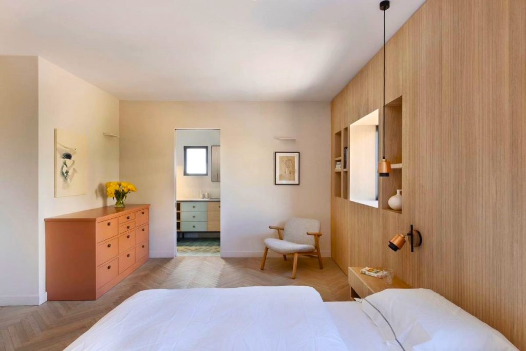 Jedna zo spální s posteľou, dreveným obložením na jednej zo stien a komodou v pastelovej oranžovej farbe.