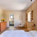 Jedna zo spální s posteľou, dreveným obložením na jednej zo stien a komodou v pastelovej oranžovej farbe.