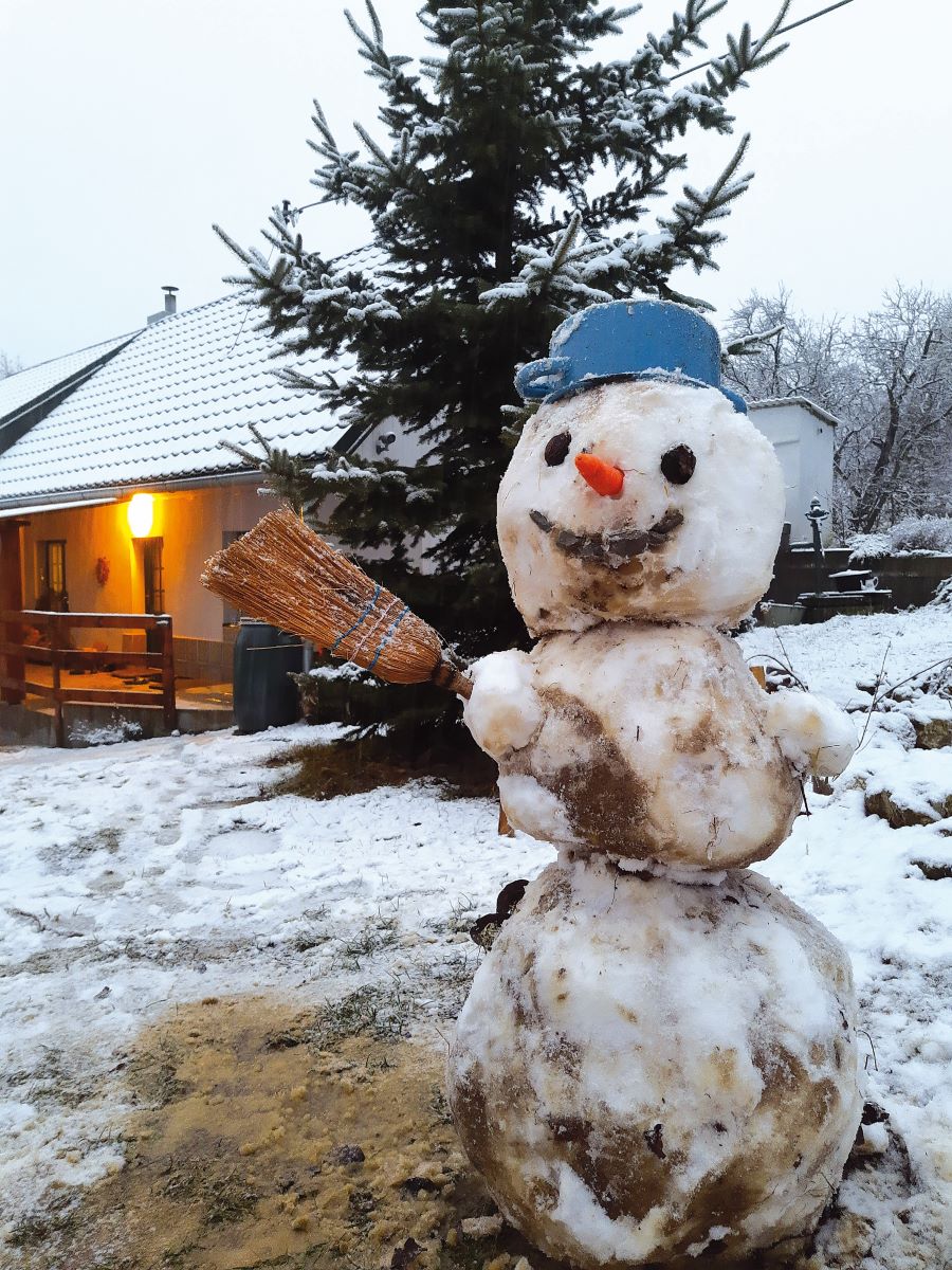 Záber na snehuliaka s metlou a hrncom v exteriéri pred domom.