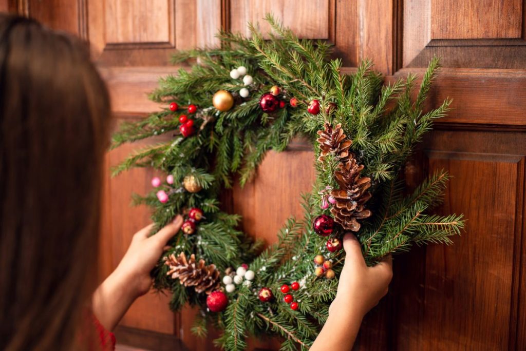 Žena zvesuje dole vianočný veniec z dverí.
