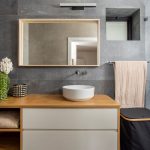 Kúpeľňa s dreveno-bielym nábytkom a sivými stenami.
