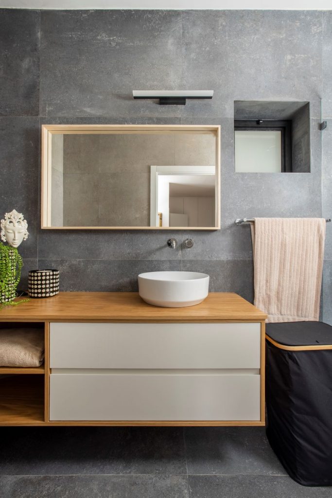 Kúpeľňa s dreveno-bielym nábytkom a sivými stenami.