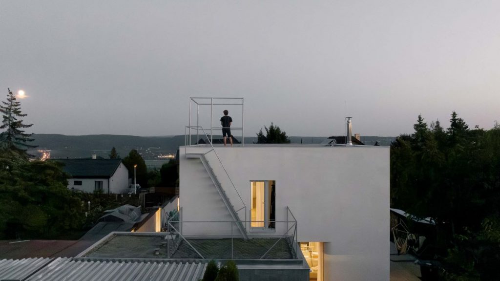 Muž na streche rodinného stojí a pozoruje mesiac.