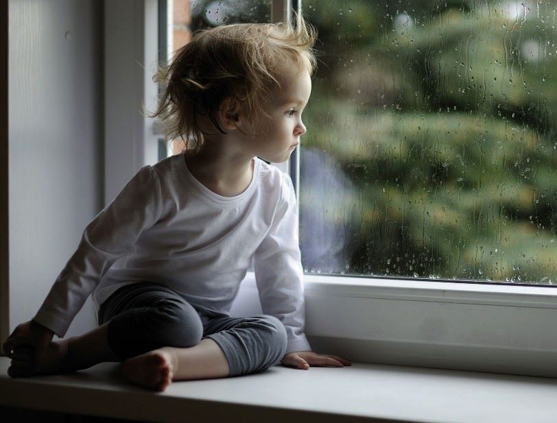 Malé dieťa sedí na parapete a pozerá sa von oknom.