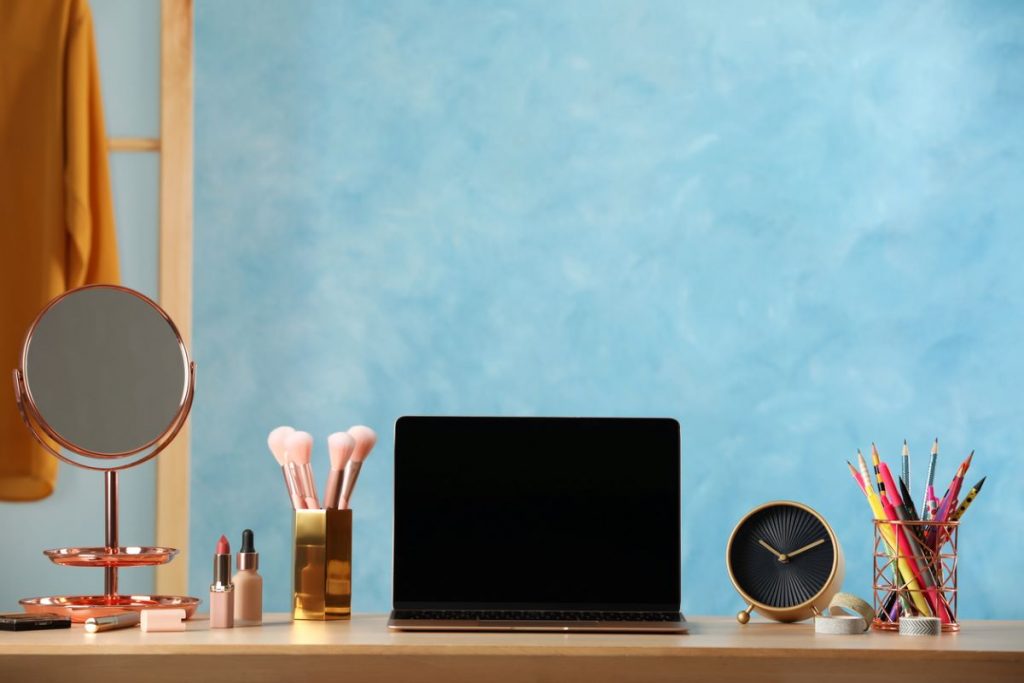 Záber na pracovný stôl s notebookom, ceruzami, budíkom a kozmetikou.