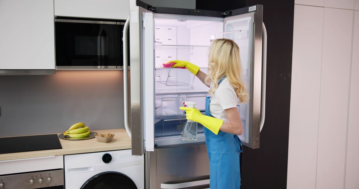 Žena v zástere umýva vnútro chladničky.