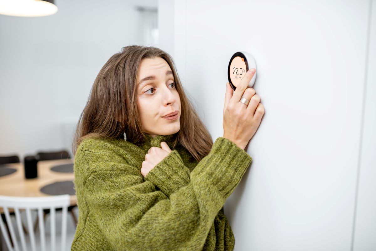 Žena nastavuje termostat na stene.