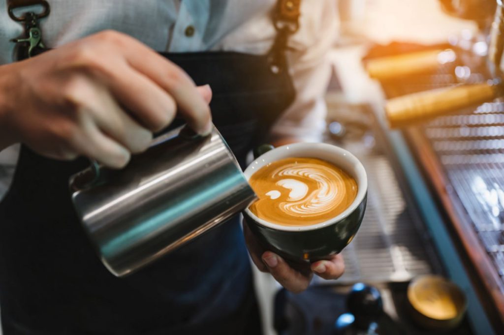 Detail na baristku vytvárajúcu latte art.