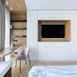 Mnimalisticky zariadená hosťovská izba v neutrálnych odtieňoch s televízorom a úložným priestorom.