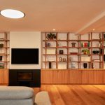 Pohľad do obývacej časti bytu s kozubom, televízokom a otvorenými drevenými policami.