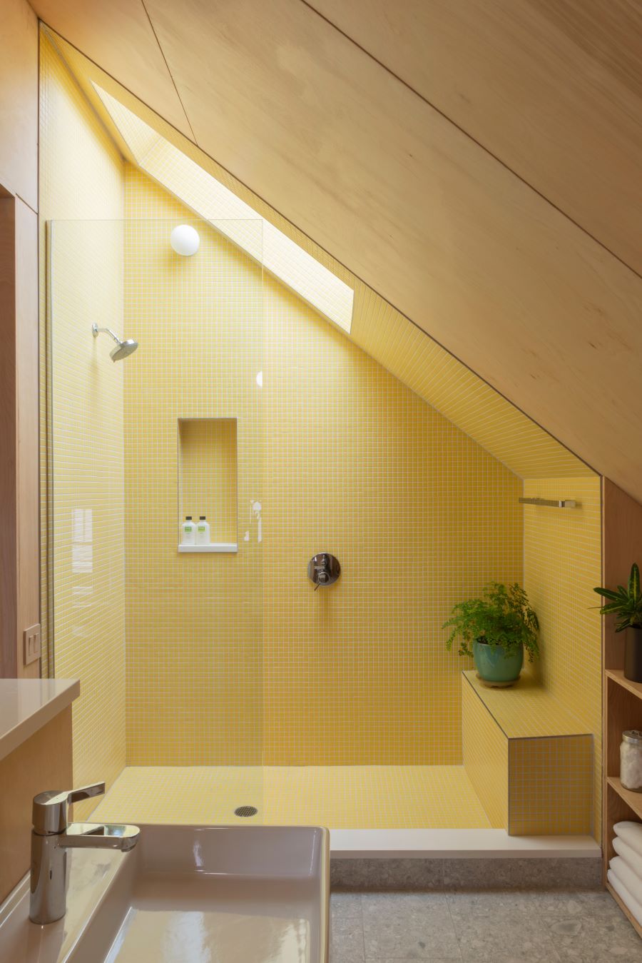 Podkrovná kúpeľňa so žltým obkladom v sprchovacom kúte.