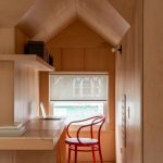 Časť interiéru s dreveným obložením, policami a červenou stoličkou.